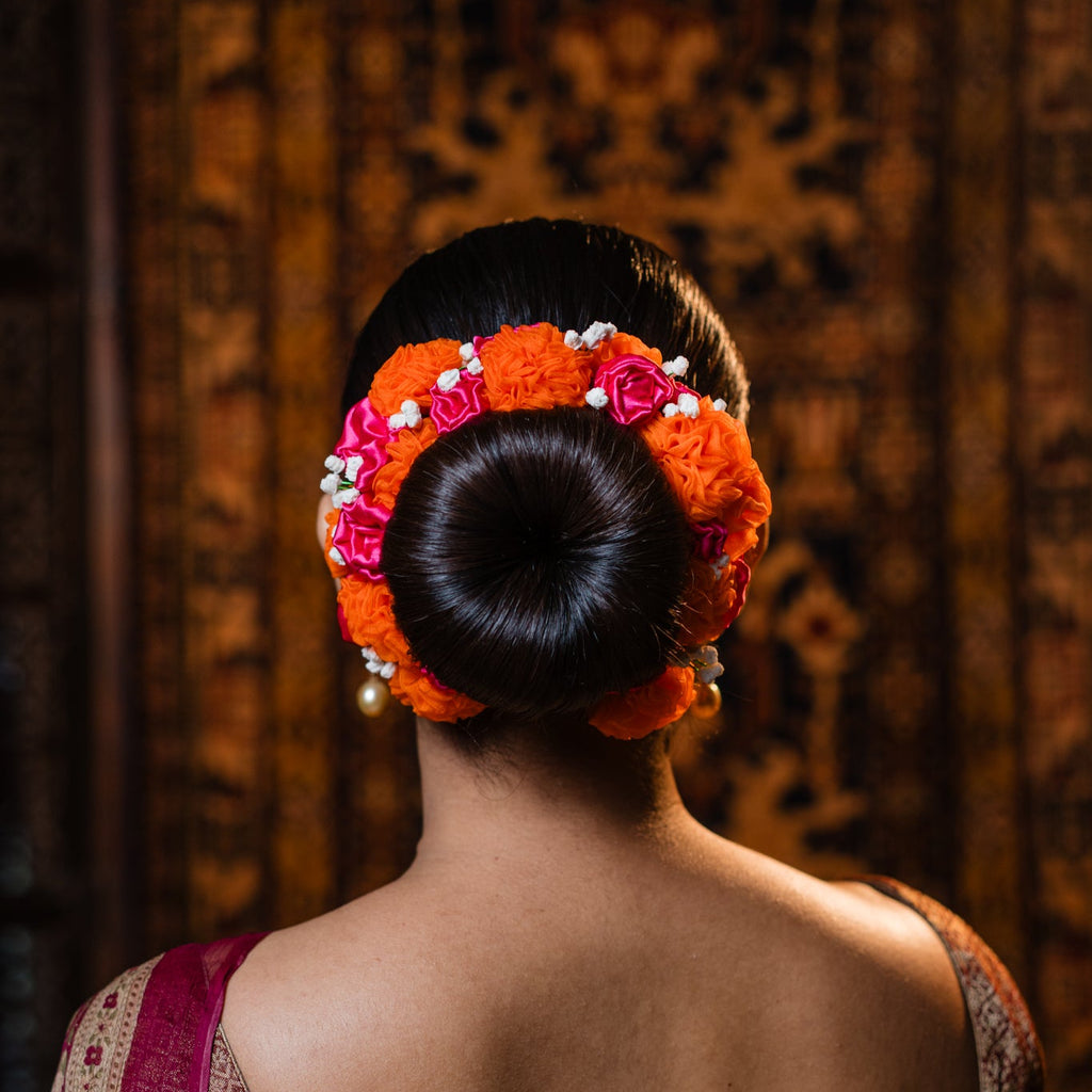 Woman with a floral hairpiece and traditional attire against a textured wall.