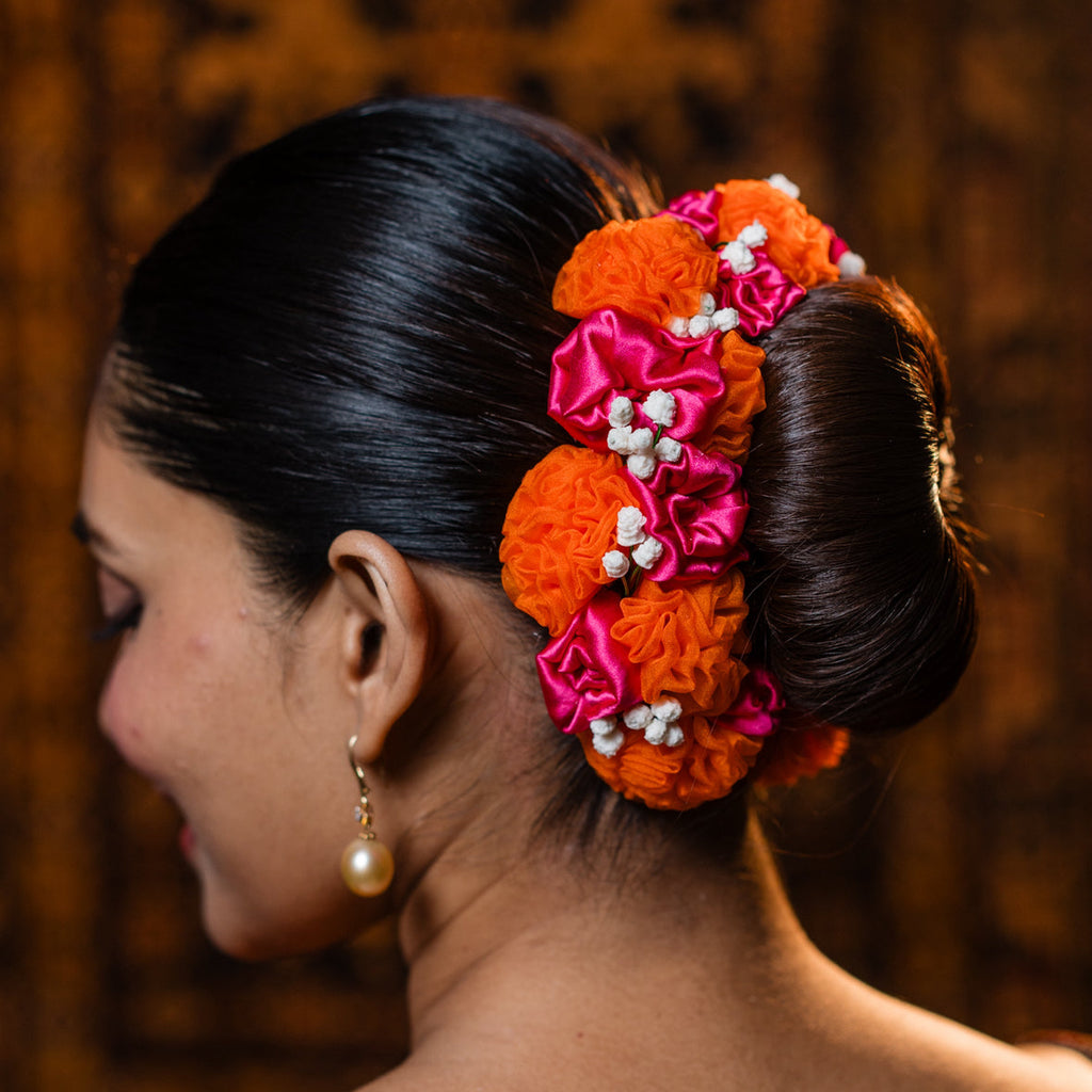 Woman with a decorative hair bun featuring orange and pink flowers against a blurred background