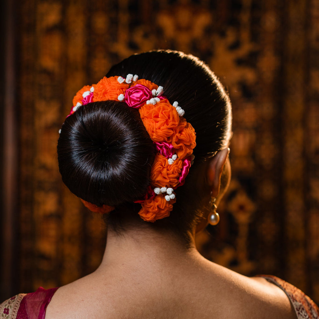 Woman with an elaborate hair bun adorned with flowers and beads, wearing a traditional saree.